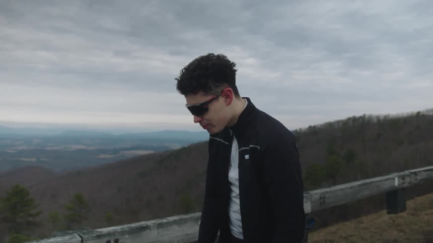 A young tired man riding a blue bicycle stops in the middle of a mountain road to take a breath