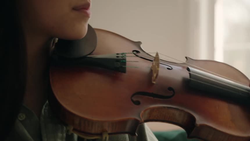 An asian smiles slightly as she brings a violin to her shoulder and begins playing