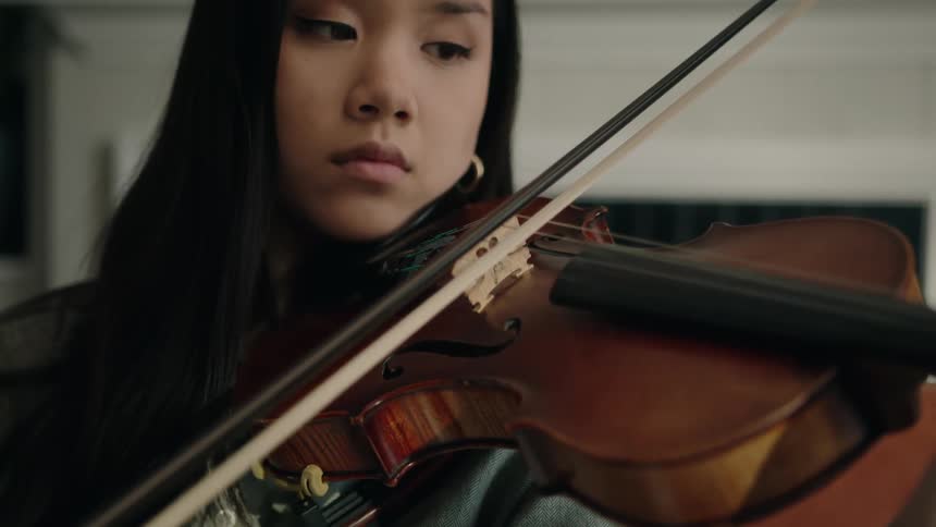 An asian woman plays a violin in a living room