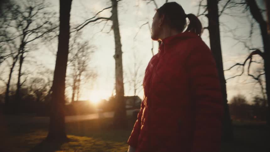 A woman in a red coat is in a rural area with some trees and she is looking around