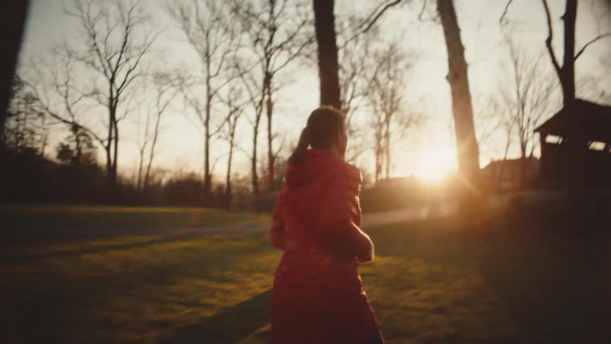 Female runner running throughthe forest at dusk in the fall