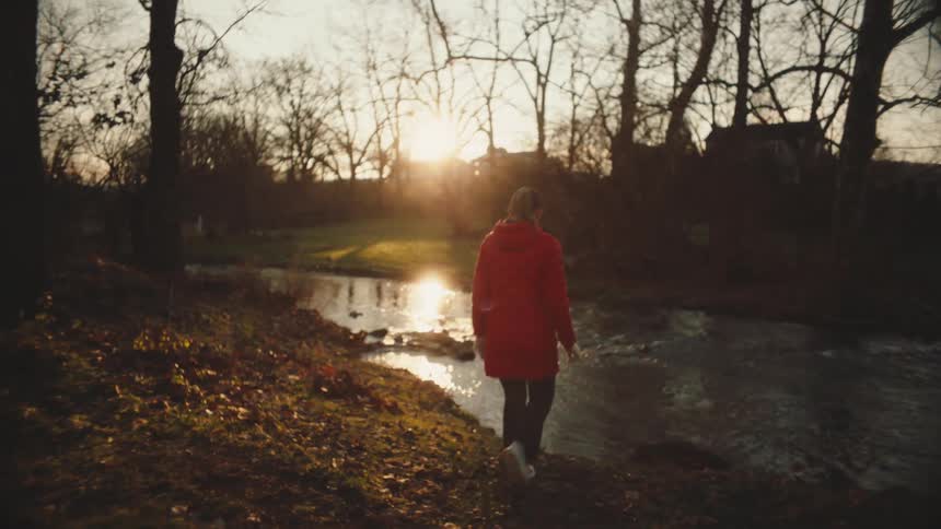Woman in a red jacket walking in a natural environment by a river