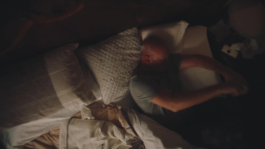 An older man awakens and exits his bed