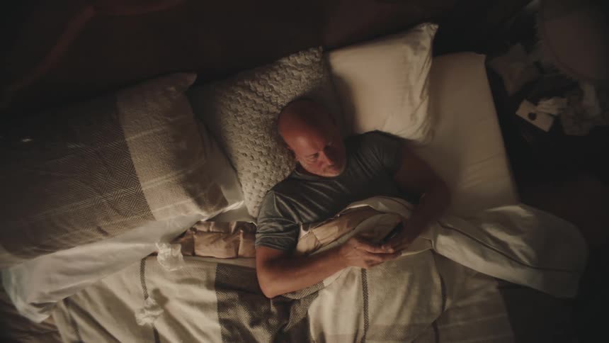 A man checks his cell phone in bed