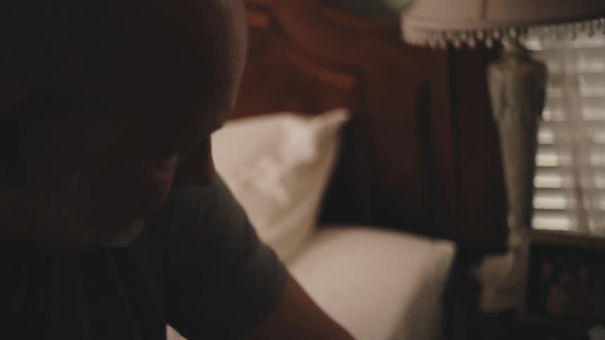 Man sitting on the bed with a dejected facial expression looking at a picture frame with photos next to him