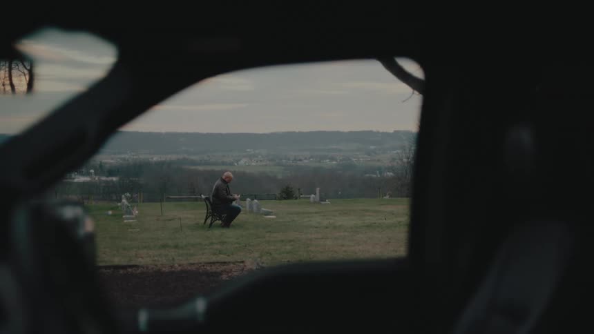 A man is sitting on a bench in the graveyard