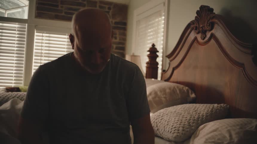 A man rolls out of bed and reaches for a smartphone on the nightstand