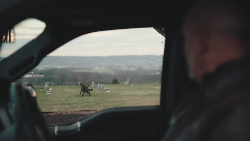 Grieving man sitting in his parked vehicle looks toward the cemetery