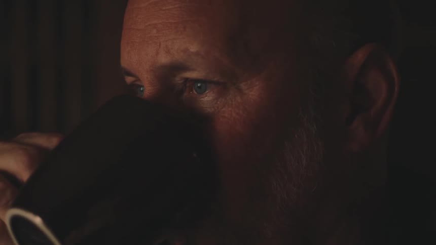 An older man looks sad as he takes a sip of drink from a cup