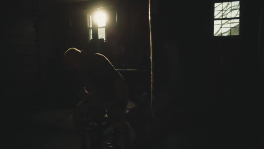 Silhouette of a man standing up from a bench inside a dimly lit home made gym