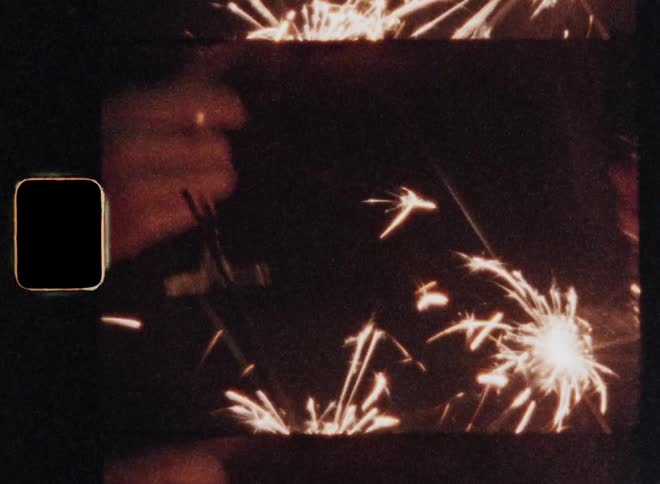 8mm close-up of the hands of unrecognisable man and a woman clinking glasses filled with champagne or alcoholic wine to celebrate together as firework sparklers burn and the sparkling candles illuminate the darkness of the night