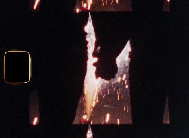Close up of the hand of a man slowly grabbing a womans hand for the first time as the silhouette of the young couple is standing in front of exploding fireworks causing bright light and lens flares while holding hands on a street at night
