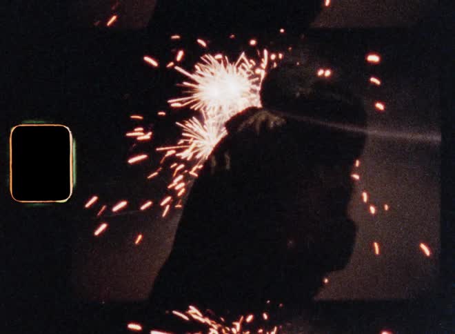 Romantic scene with positive vibes and happy feelings of a couple hugging on the street at night while firework explodes in the background and the sparkles illuminate their moving silhouettes on S8 film