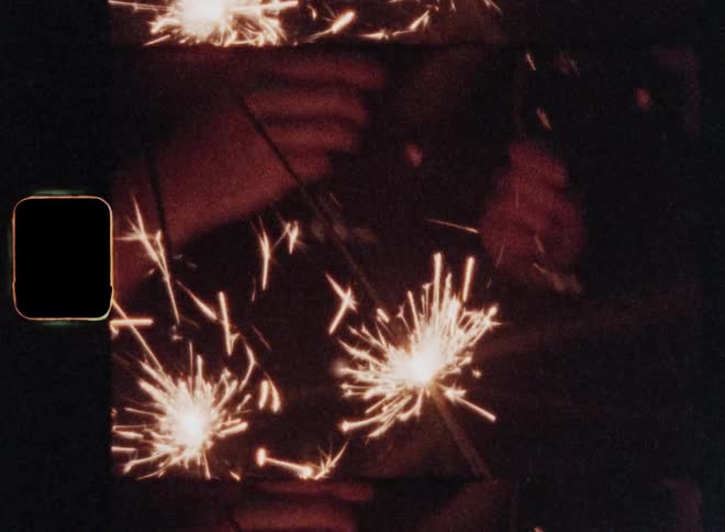Super 8mm close-up of the hands of two people holding sparklers and champagne glasses as they clink their drinks while toasting and sparks flying around them while enjoying a festive drink at night time celebration with a happy mood