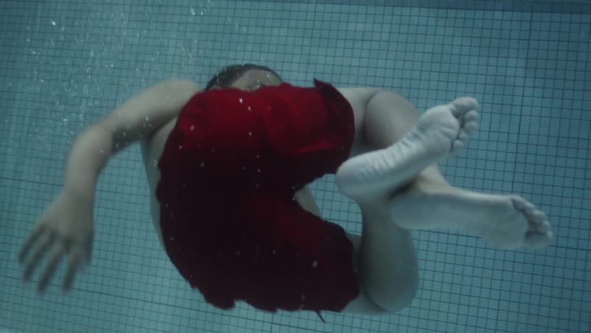 A black child holds his nose and goes under the water in a pool