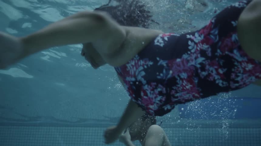 A family swimming underwater in a pool with sunlight filtering through the water