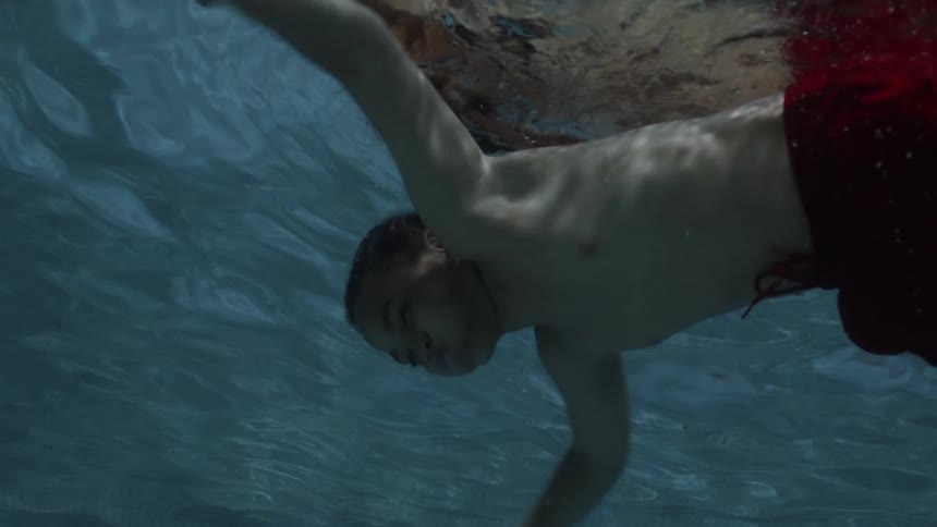 A young black boy dives underneath the surface of a pool