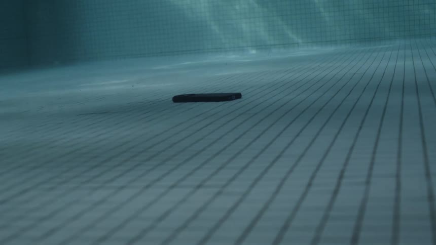 Close up of a hand reaching to pick up a smartphone from the bottom of a swimming pool