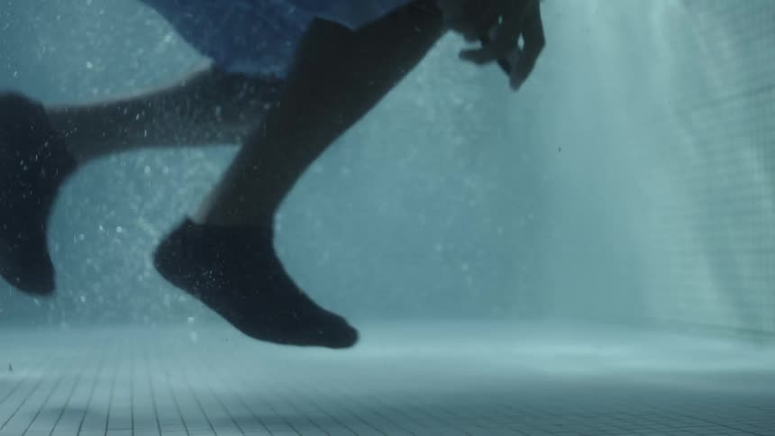 A man falling to the bottom of a pool in order to retrieve his phone