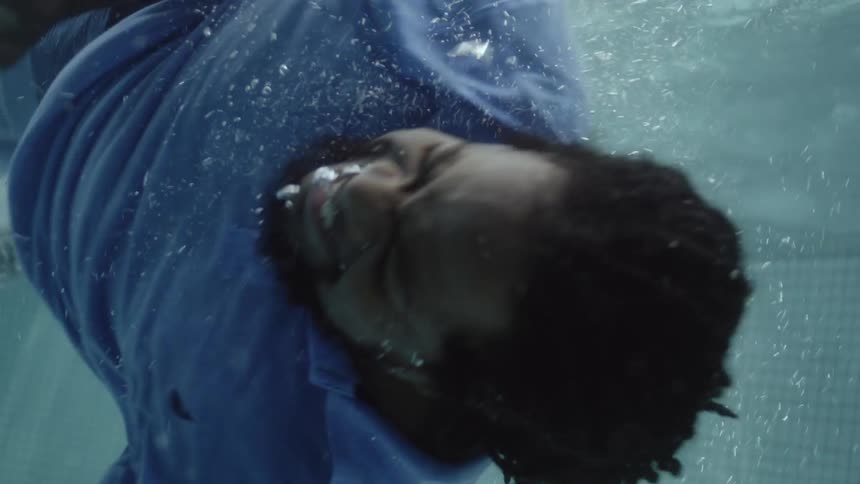 A fully clothed man jumps in the pool and swims underwater