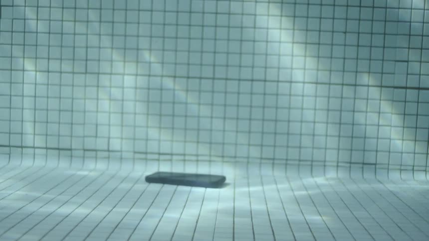 A phone falls to the bottom of a pool and a person picks it up