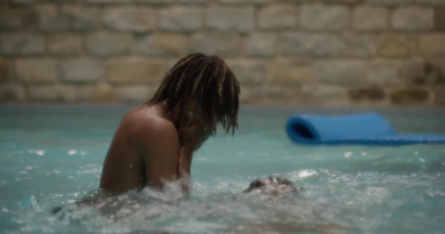 A teenage black boy dunks a younger black boy in a swimming pool