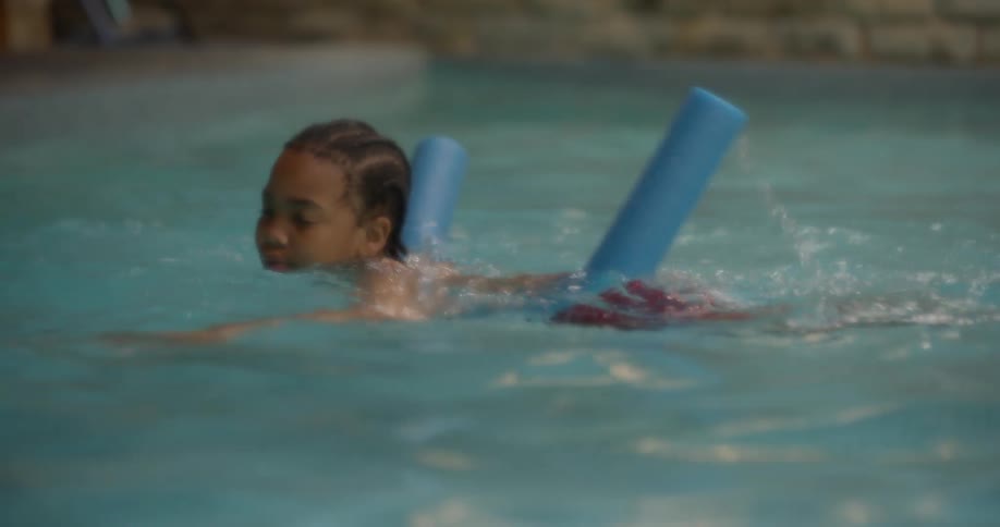 A young boy splashes over to a flotation device in a swimming pool