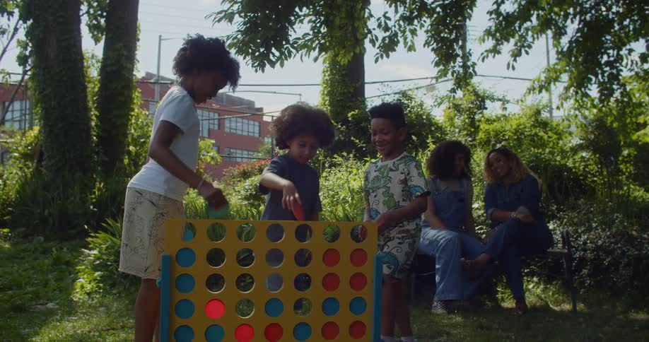 Two mothers sit while three young children play jumbo Connect Four