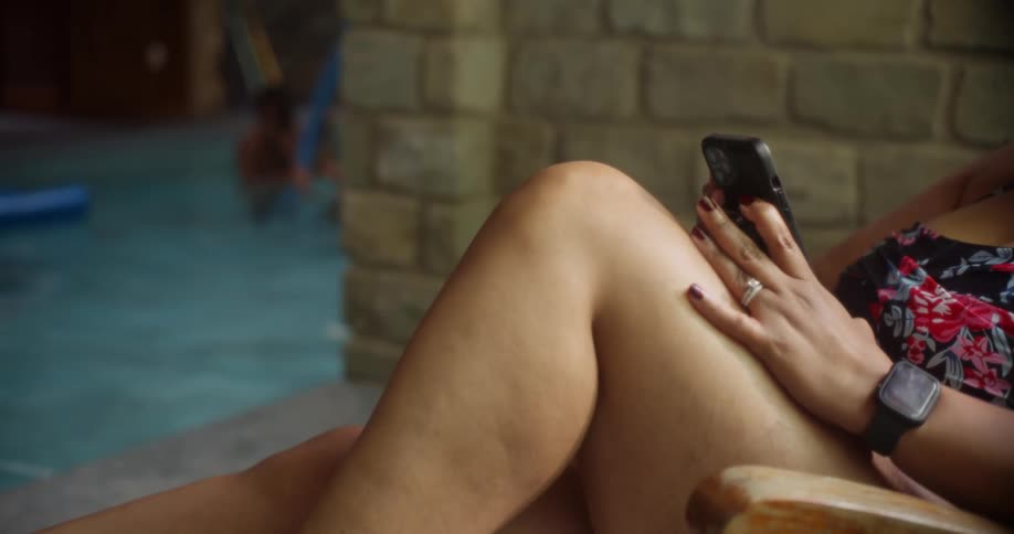 Woman sitting on a chair using her smartphone and in the background two children playing in a pool