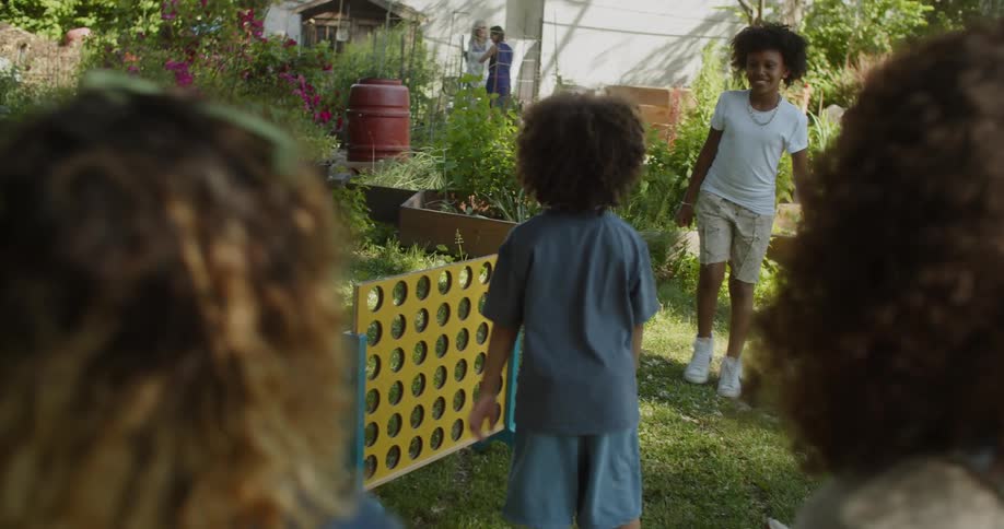 Two moms watching in the background as three children play with each other in a garden