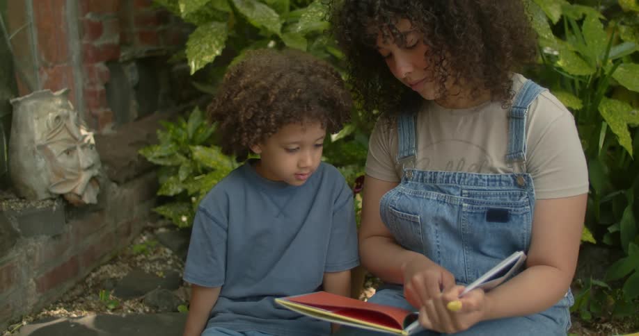 Woman and a boy sitting in a garden reading a book
