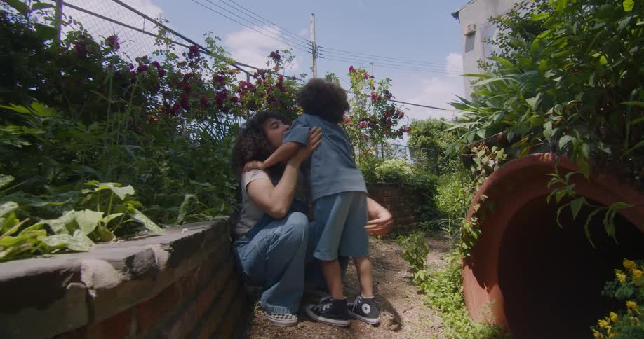 A woman crouches down waiting for her little son to come out of a tube and he comes out and gives her a hug