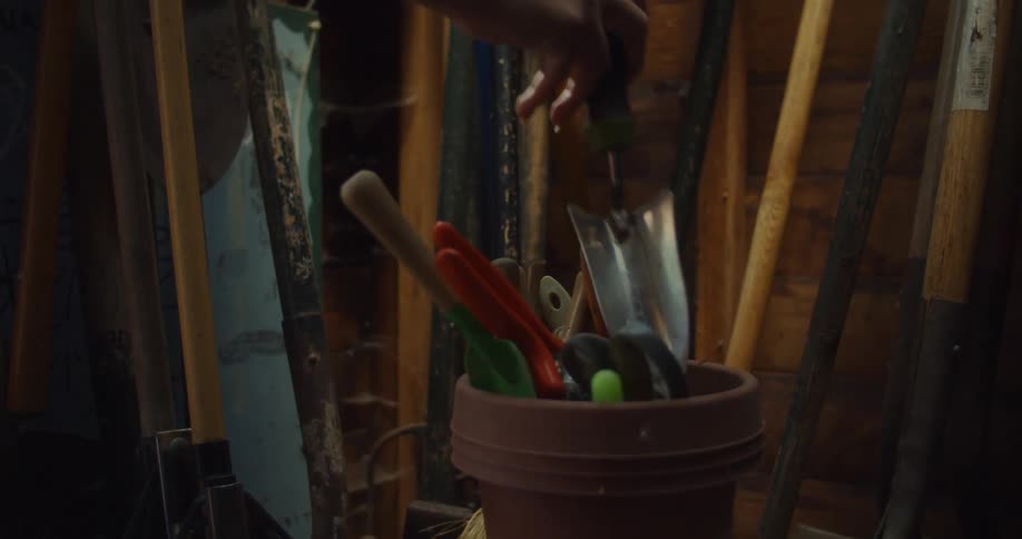 A gardener removes a trowel from a bucket of gardening tools