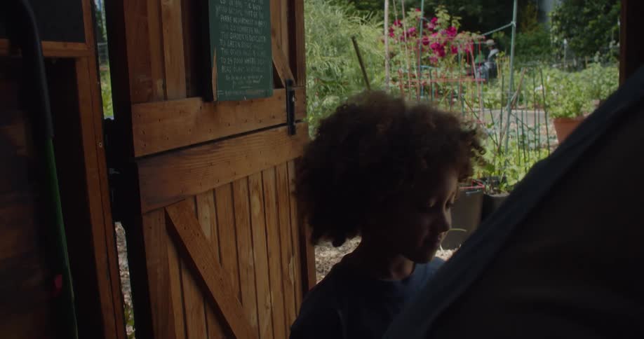 A young woman and a child enter a small wooden tool shed in a garden