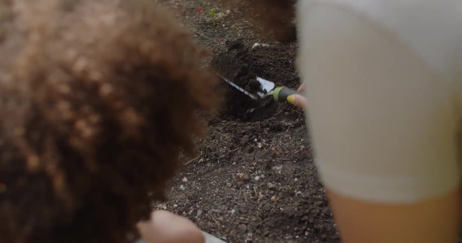 Woman next to a little boy holding a trowel and removing soil