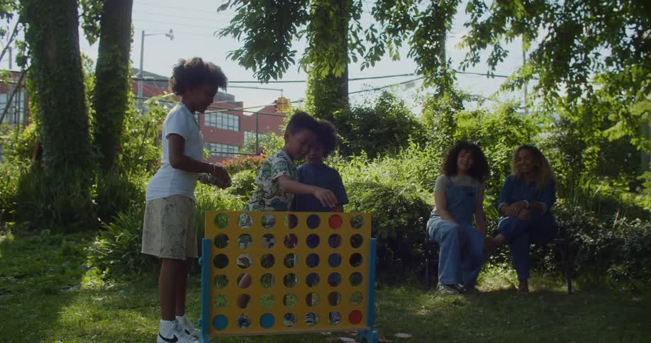 Two women sitting in a garden and three children playing in front of them