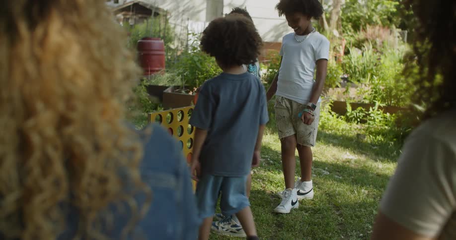 Two women sit watching three children in a garden playing a game