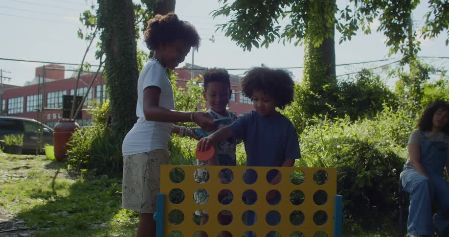 Three kids play a game in a garden as their mothers watch