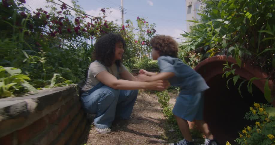 Little boy coming out of a tunnel and going to hug his mother while they are in a garden