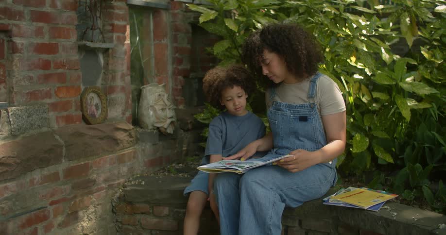 A mother and her son read a book together while sitting in a park