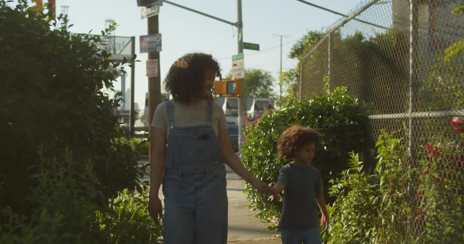 Mother and son walking on the sidewalk holding hands visiting a community garden in the city