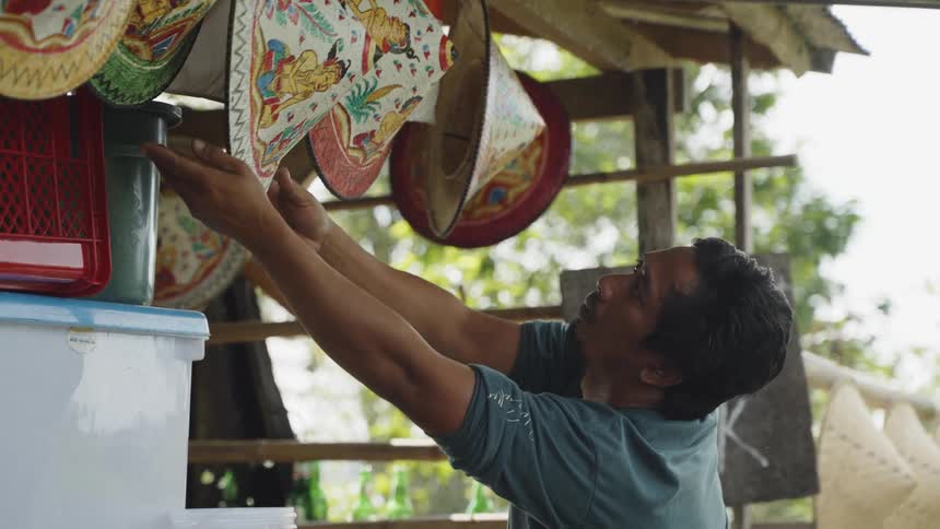A man arranging colorful rice paddy hats at his roadside stall in Bali