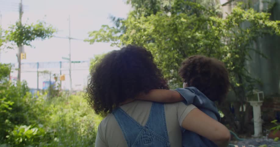 A young woman carrying a child as they explore in a city garden