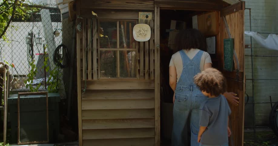 Woman and a little boy entering a wooden tool shed in a backyard