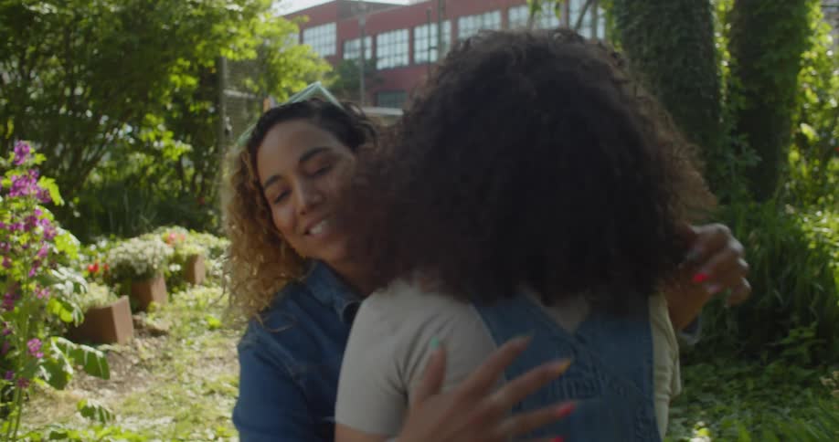 A mom and two kids walk into a garden and the mom greets her friend with a hug