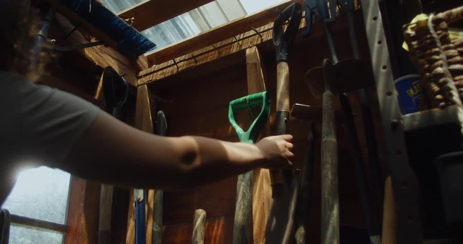 A woman reaches for a shovel in a tool shed