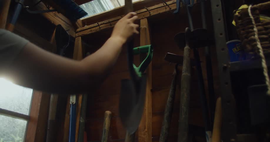 A person takes a shovel from a small tool shed