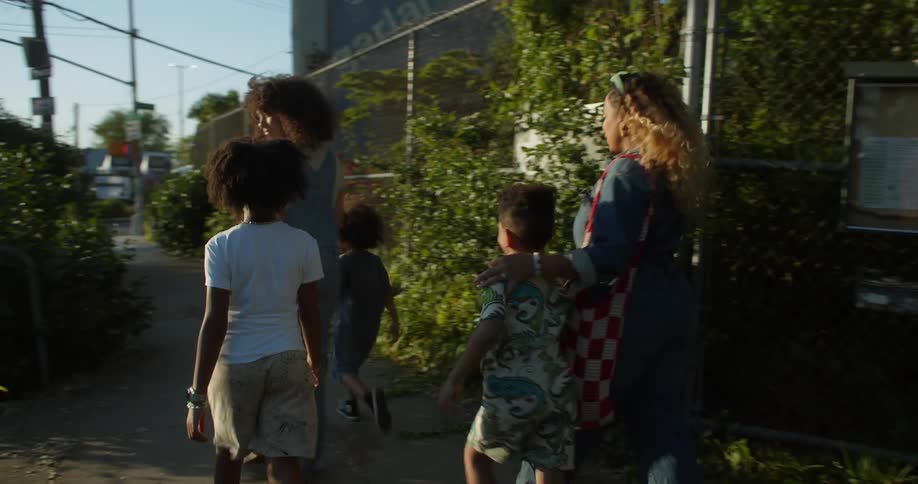 Two women and three children walk out of the community garden to the city sidewalk