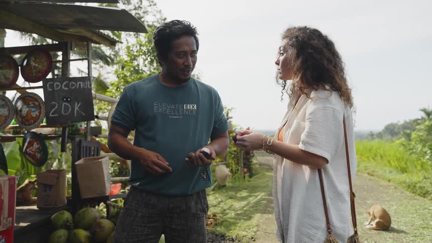 A woman samples food at a roadside stand while speaking with the owner