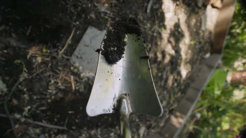 Close up of a metal garden trowel moving soil with its blade